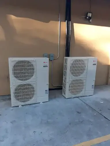 Two white outdoor HVAC condenser units with dual fans mounted on concrete pad with refrigerant lines