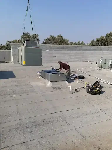 Technician installing rooftop HVAC unit with ductwork on commercial flat roof