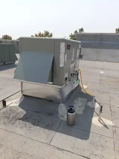 Gray commercial HVAC unit mounted on concrete pad with yellow electrical conduit and disconnect switch on flat roof